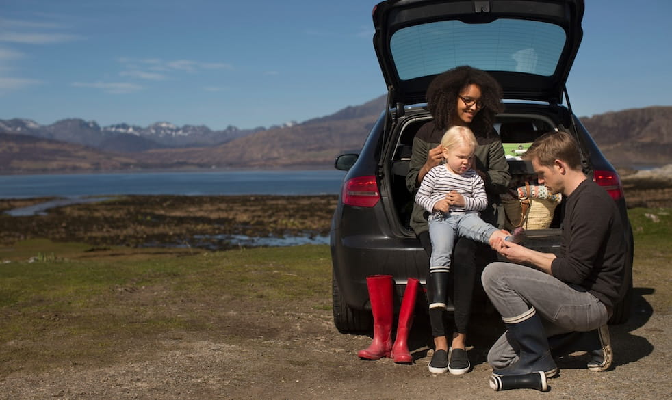 Parents helping son change shoes sitting in the boot of the car